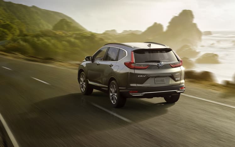 Rear driver-side view of the 2022 CR-V Hybrid Touring in Modern Steel Metallic, driving along a coastal highway.