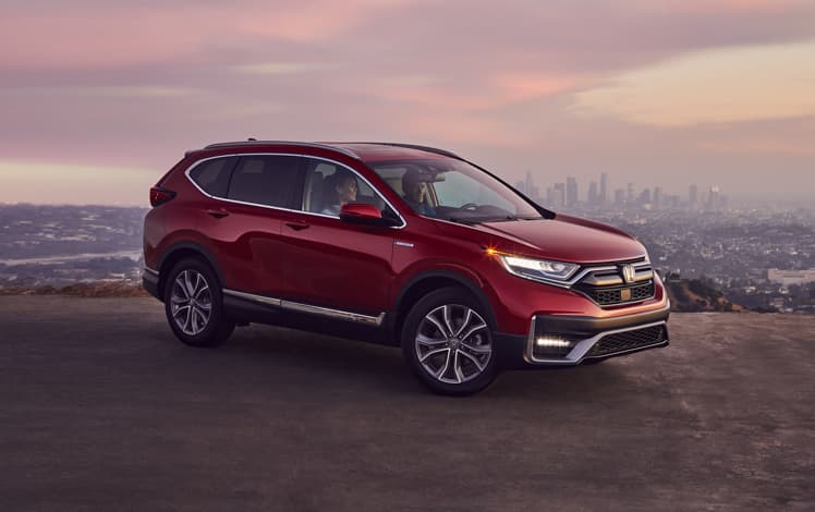 Front passenger-side view of the 2022 CR-V Hybrid Touring in Radiant Red Metallic, parked at a city overlook at night.