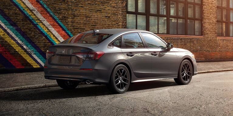 2027 Honda Civic Sedan Sport in Meteorite Gray Metallic rear three-quarter view parked on a city street (Compact Sedan)